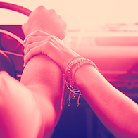 A man has hand on the steering wheel of a car while a woman lovingly holds his wrist.