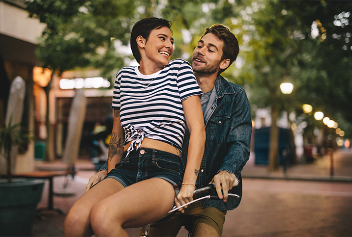 A woman sitting on bicycle handlebars smiles back at the man riding the bike.