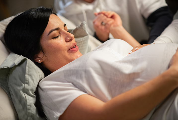 A woman in labor breathes with her eyes closed while holding hands with another person.