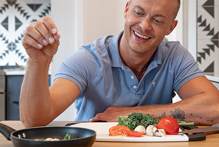 A man is putting a pinch of seasoning into a pan while cooking.