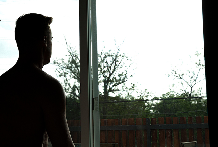 A man living with erectile dysfunction looks out the window in a silhouette. 