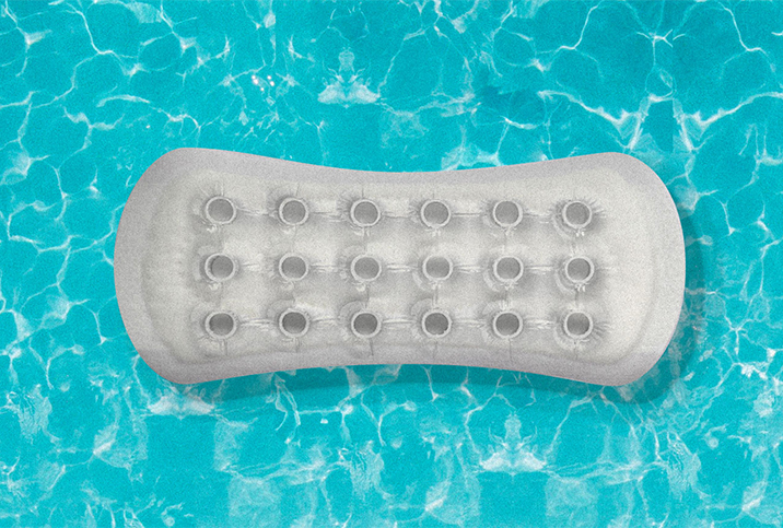 A pool floaty shaped like a menstrual pad, floats in a blue pool.