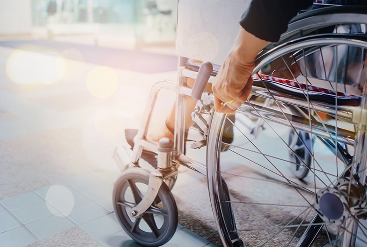 A person sits in a wheelchair and holds the frame with the sun shining down on them.