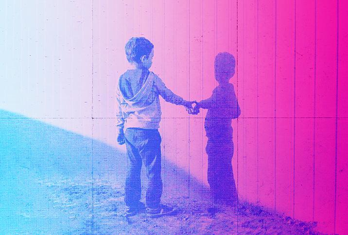 A little boy reaches out to touch his shadow on a pink wall. 