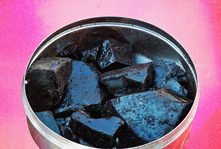 Pieces of Shilajit sit inside a tin against a pink background.