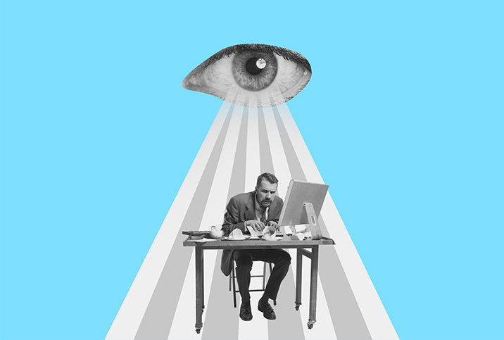 An eye beams down on a stressed man working at his desk.