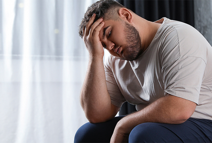 A sitting man has his elbow propped up on his knee and his head in his hand.