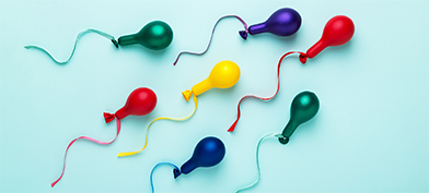Multiple colors of barely blown up balloons have a string tied on the end to look like sperm.