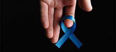 An upside down hand holds a blue ribbon on its index finger.