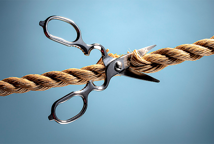 A pair of scissors is cutting a thick brown rope.