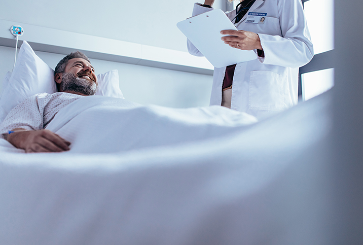 A man smiles in a hospital bed while looking up at his doctor after a vasectomy.