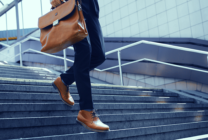 A person walks down the stairs outside while holding a briefcase.