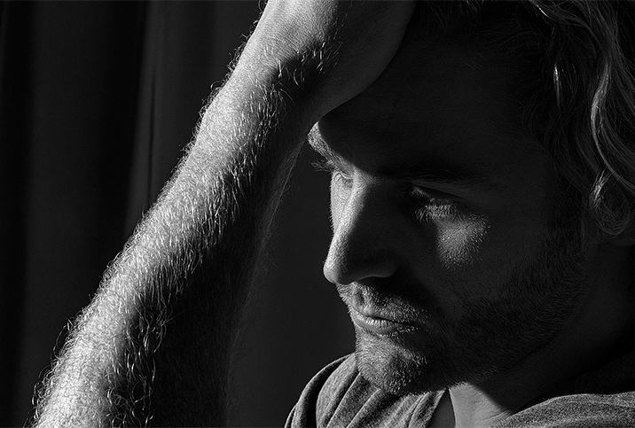 A close up of a man looking concerned while holding his head against his hand.