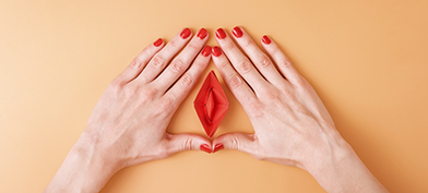 Two hands with red painted nails surround frame a vulva-shaped origami. 