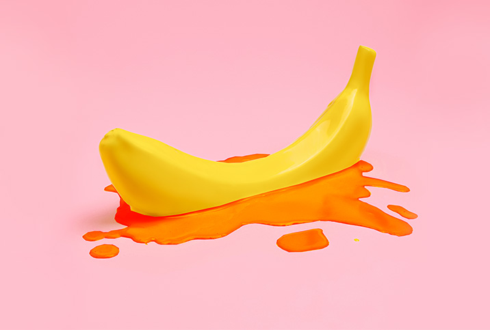 A banana sits in a small pool of blood on a pink background.