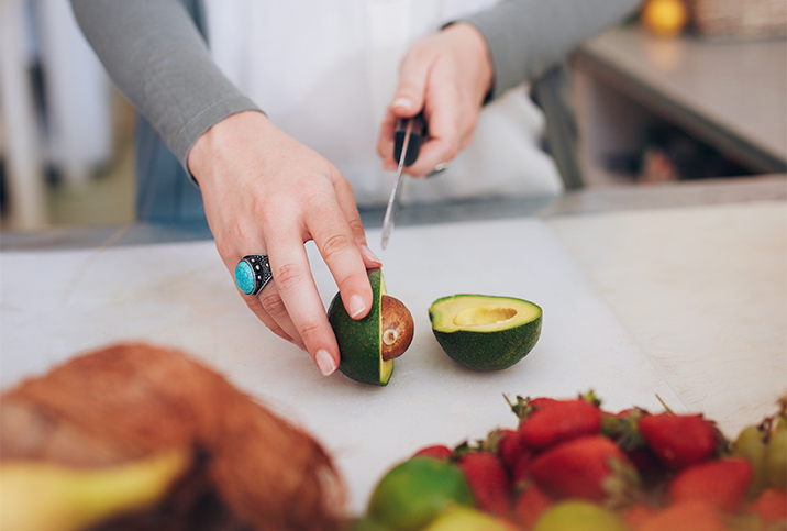 A person cuts an avocado on a cutting board.