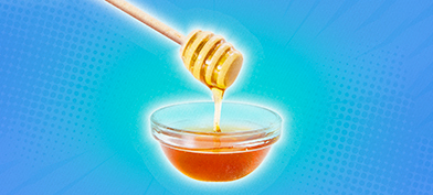 Honey is falling down from a dipper into a small dish against a blue background.