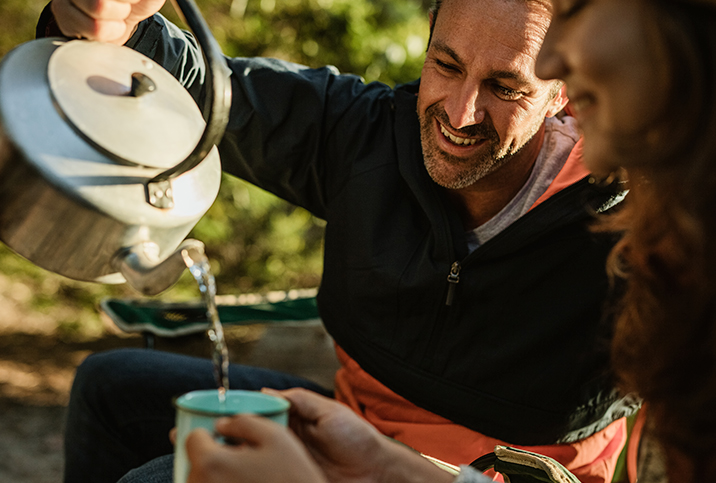 A man pours hot water from a kettle into a mug for green tea.