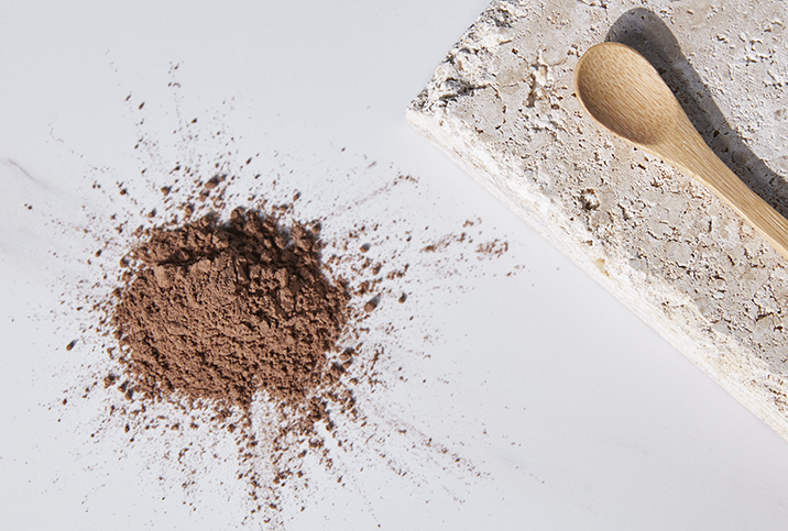 A wooden spoon on a stone plate lies next to a pile of brown powder.