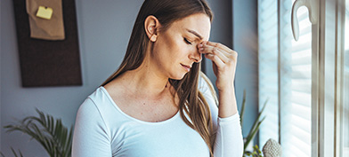 A pregnant woman with a migraine holds her belly and pinches her nose between her eyes.