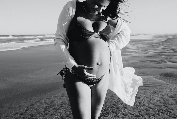 A black and white photo shows a pregnant person looking down at their belly.