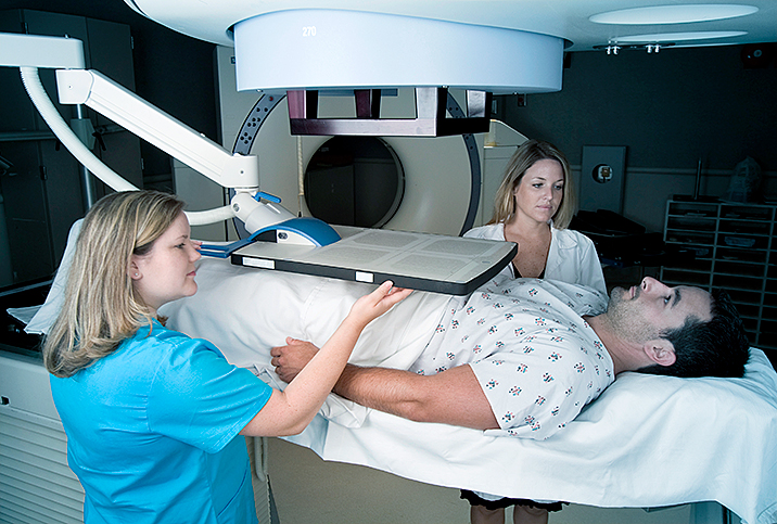 A man with prostate cancer lays under a radiation machine with two technicians next to him.