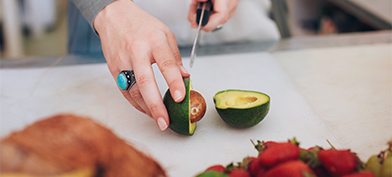 A person cuts an avocado on a cutting board.
