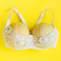 Two honeydew melons fill out a white, lacy bra on a yellow background.