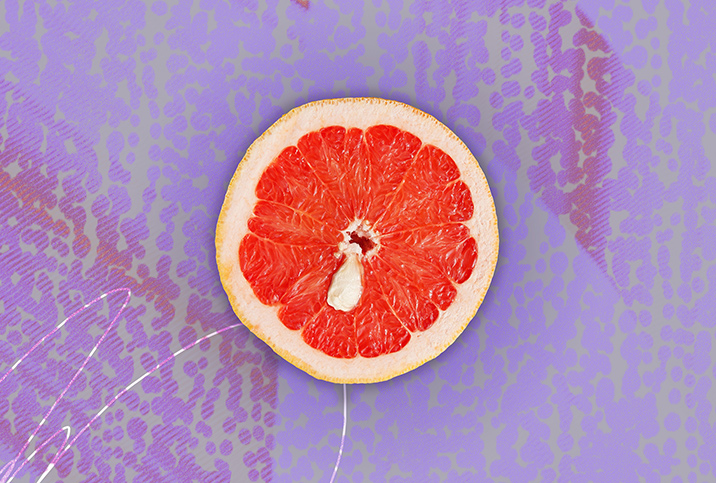 Half of a grapefruit is against a purple background and has a white cyst towards the middle of it.
