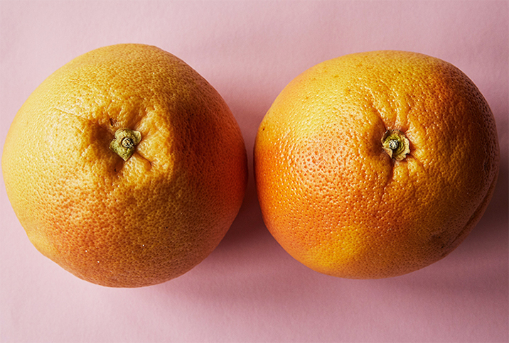 Two oranges sit side by side, resembling breasts. 
