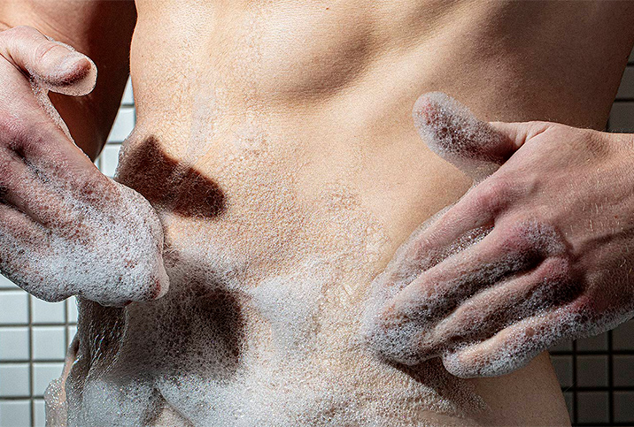 A man cleans his torso with soap and creates bubbles on his hands.