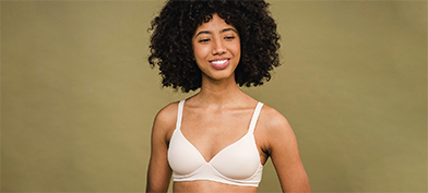 A woman wearing a white bra looks forward, smiling.