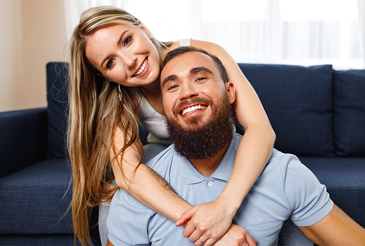 A smiling woman wraps her arms around a smiling, bearded man. 