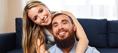 A smiling woman wraps her arms around a smiling, bearded man. 