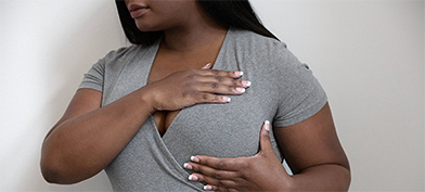 A woman in a grey shirt touches the top and bottom of her left breast.