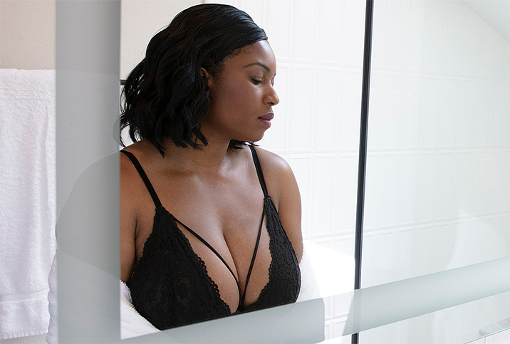 A woman stands in front of a mirror in a black bra.