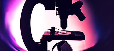 A microscope is backlight by a circle of white light that fades out to pink and purple.