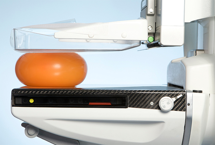 A orange, plastic ball gets compressed in a mammogram machine. 