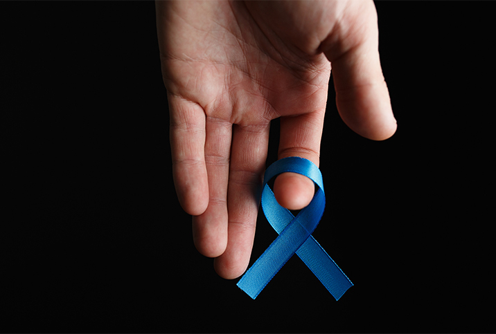 An upside down hand holds a blue ribbon on its index finger.
