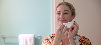 A woman holds a tissue to her face as she cleans it.