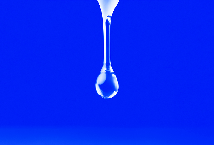 A clear drop of liquid is falling against a bright blue background.