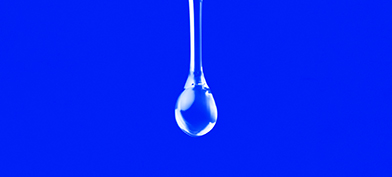A clear drop of liquid is falling against a bright blue background.