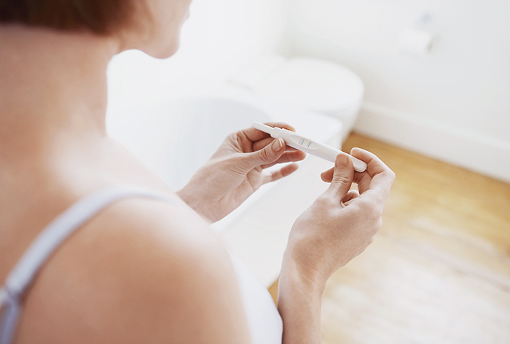 A woman looks down at a pregnancy test in her two hands.