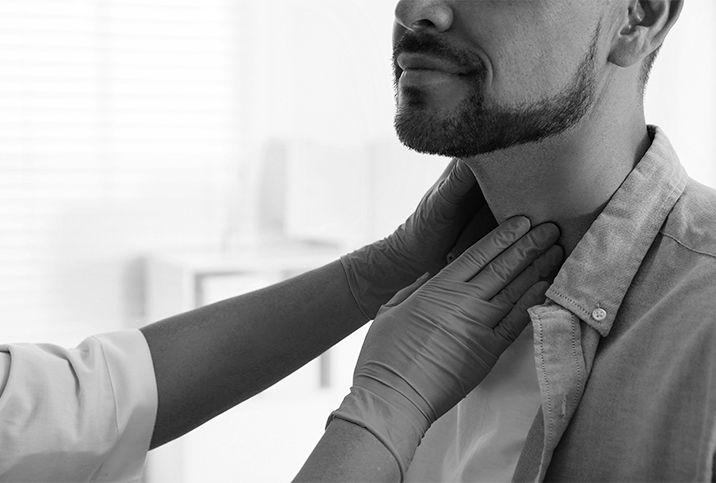 Two gloved hands palpate a bearded man's neck.