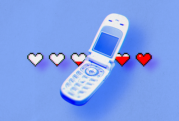 An old flip cellphone is open with a line of white hearts behind it that are filling up with red.
