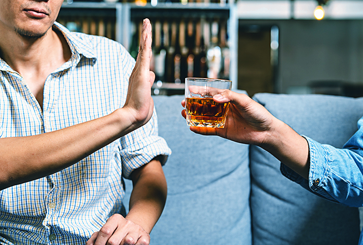 A man holds his hand up to refuse an alcoholic drink being offered to him.