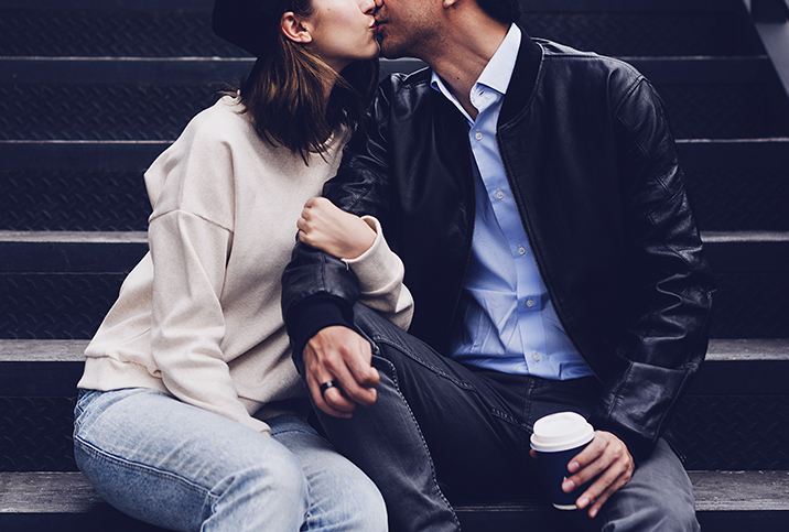 A man and woman kiss and embrace while sitting on steps outside.