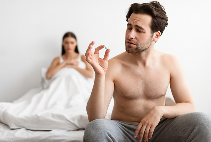 A man sitting on a bed holds up a prescription drug that could cause a low sex drive.