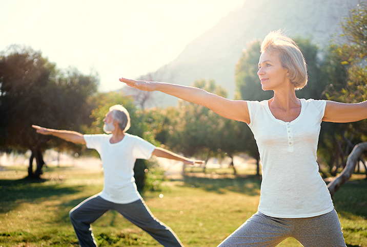 Two seniors do stretches in a field under the sunlight.