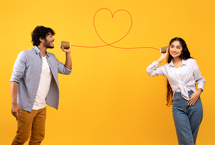 A man talks into a cup with a string in the shape of a heart leading to another cup that has a woman listening.